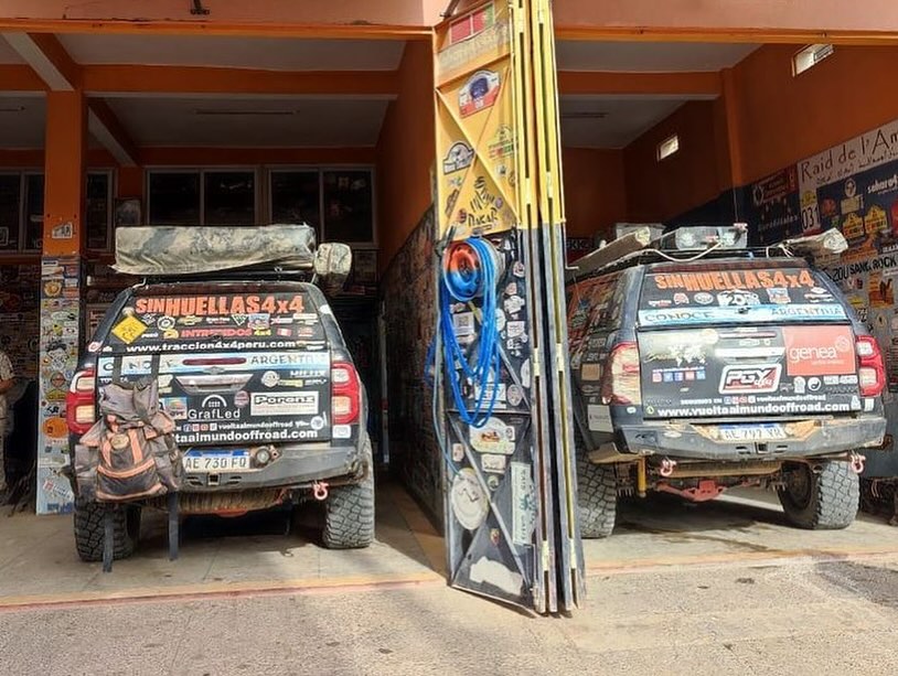 Both Argentinian SinHuellas 4x4 Toyota Hilux trucks side by side inside Garage Iriki Zagora, rear view with world-tour stickers