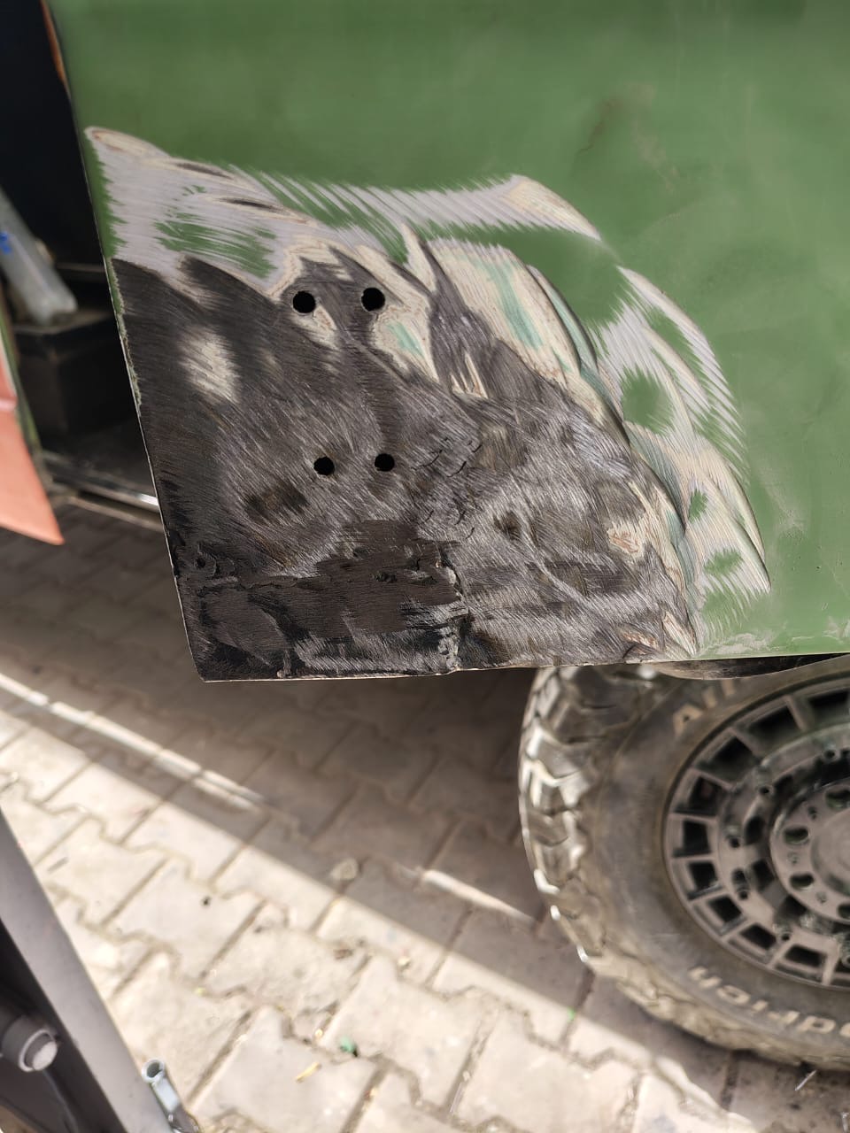 Sanded lower rear corner of the green VW camper with fresh weld patches and drilled holes for new fittings