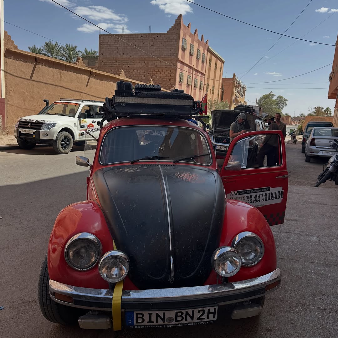 Red rally VW Beetle #109 'Rallye Macadam / Off The Beaten Track' with German plates parked in front of Garage Iriki Zagora, Morocco