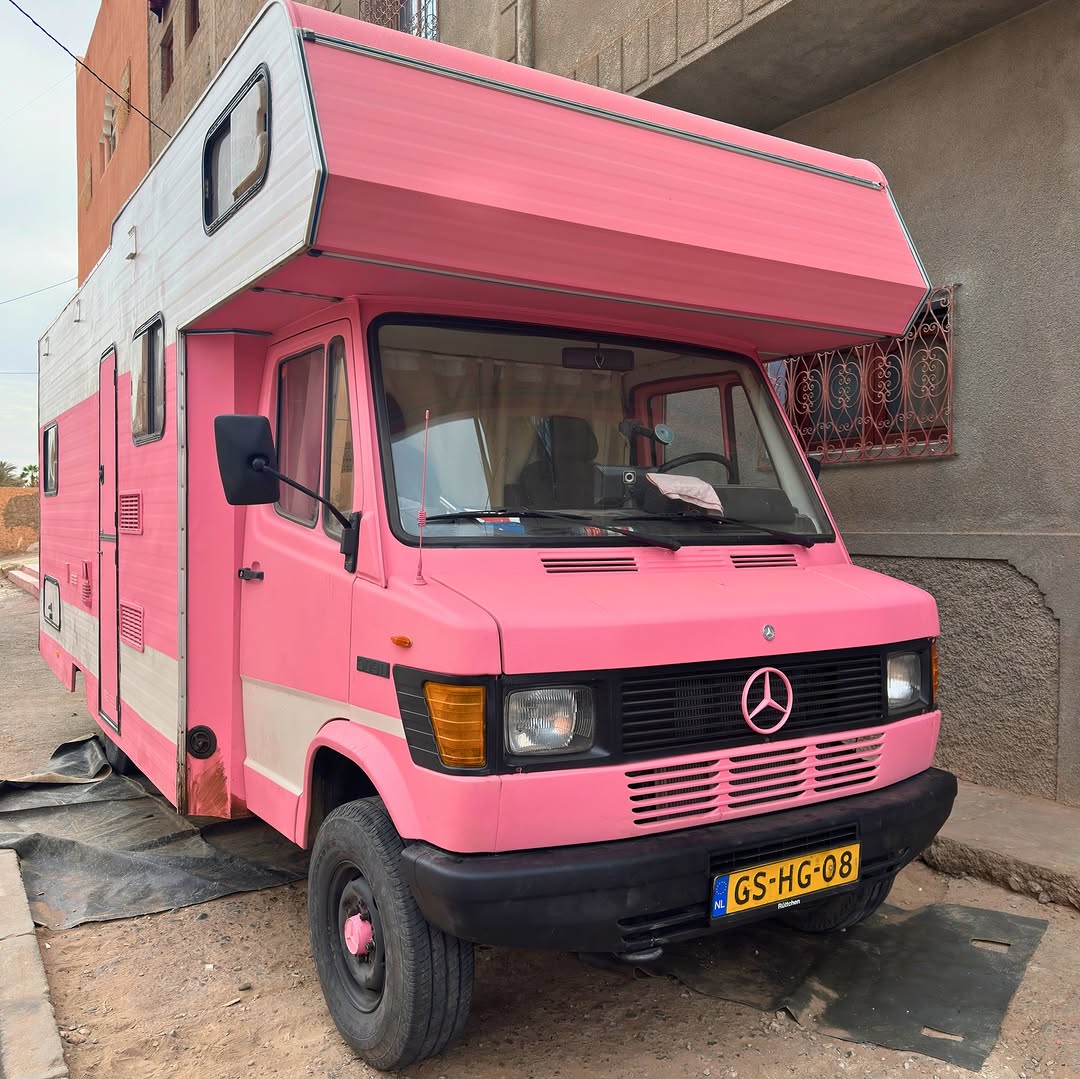 Pink Dutch Mercedes-Benz 407D camper parked outside Garage Iriki in Zagora, Morocco, after suspension lift