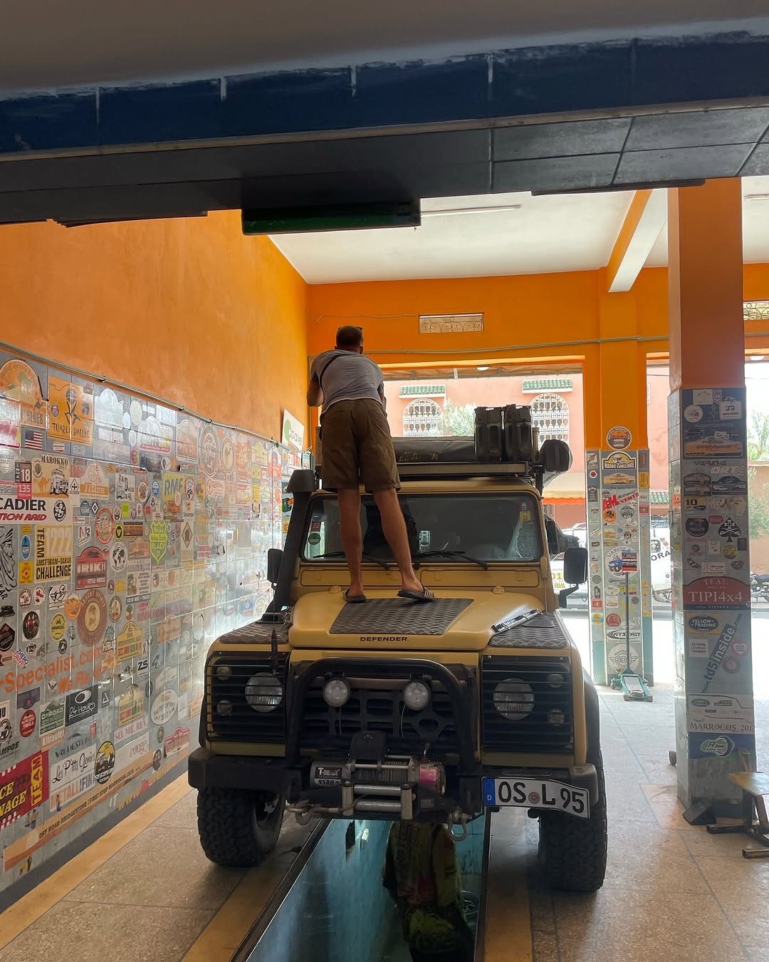 Owner standing on the hood of the yellow Defender 110 inside Garage Iriki, sticker-covered walls behind