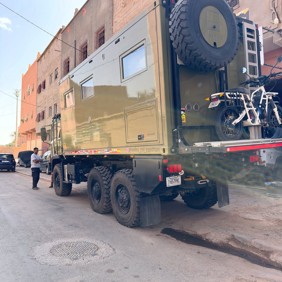 Rear view of the Endless Trail Expeditions Acela 6x6 with spare tire, e-bike rack and country flag stickers
