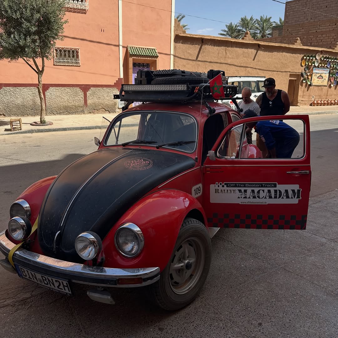 Classic red Volkswagen Beetle rally car with roof rack, jerry cans and Moroccan flag on a Zagora street